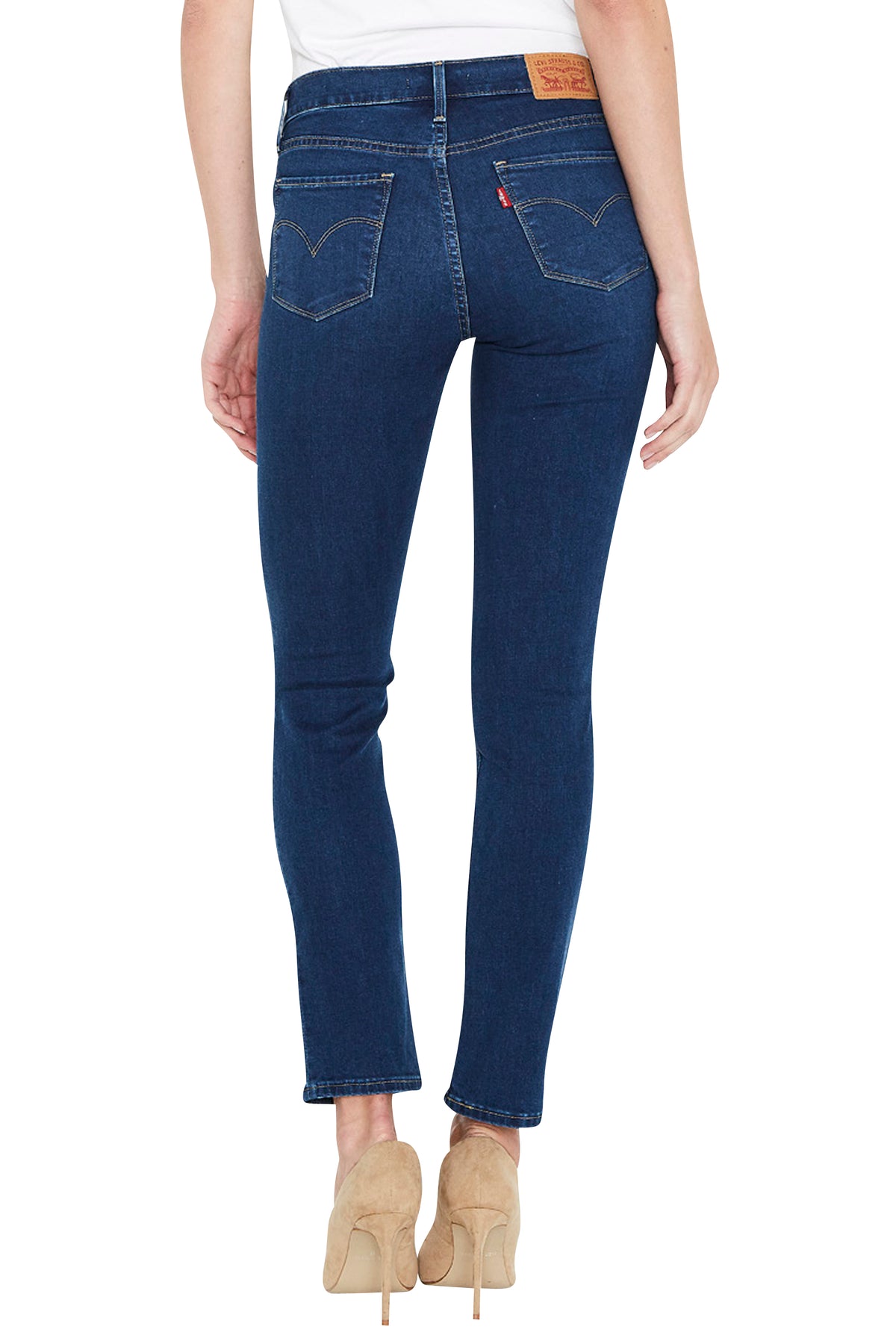 Rear view of a model wearing dark blue skinny jeans with beige high heels, shown against a plain white background.