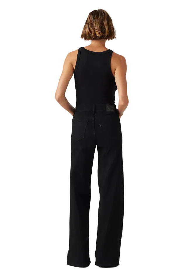Person wearing a black sleeveless top and black pants on a light gray background