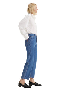Person wearing a white shirt and blue jeans standing against a white background.