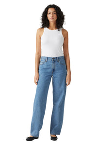 Woman wearing a white sleeveless top and blue jeans on a white background