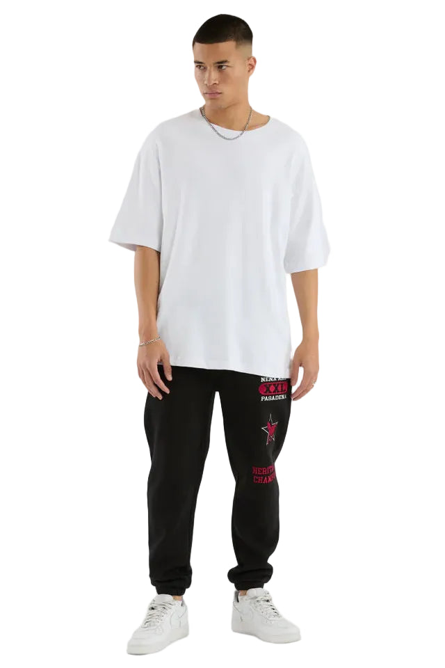 Man wearing a white oversized t-shirt and black sweatpants with red text on a white background