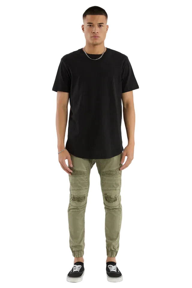 Man wearing a black t-shirt and green distressed jeans on a white background