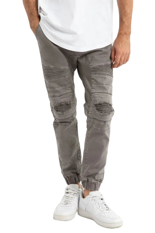 Person wearing gray distressed pants and white sneakers on a light gray background