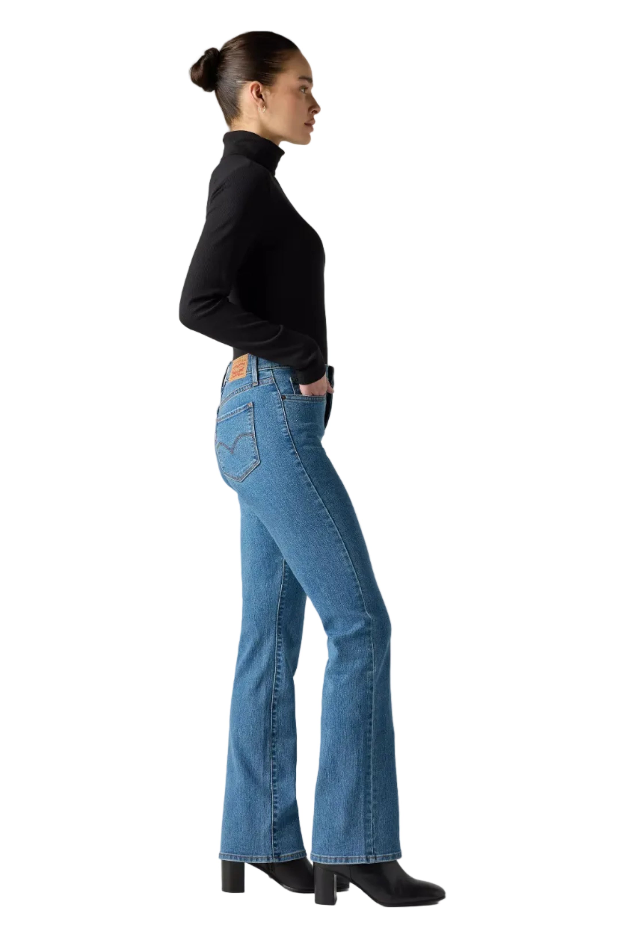 Woman wearing blue jeans and a black turtleneck against a plain background