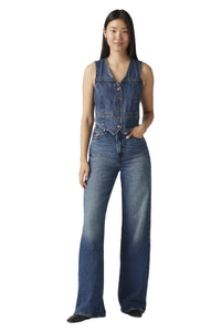 Woman wearing a denim vest and jeans on a plain background