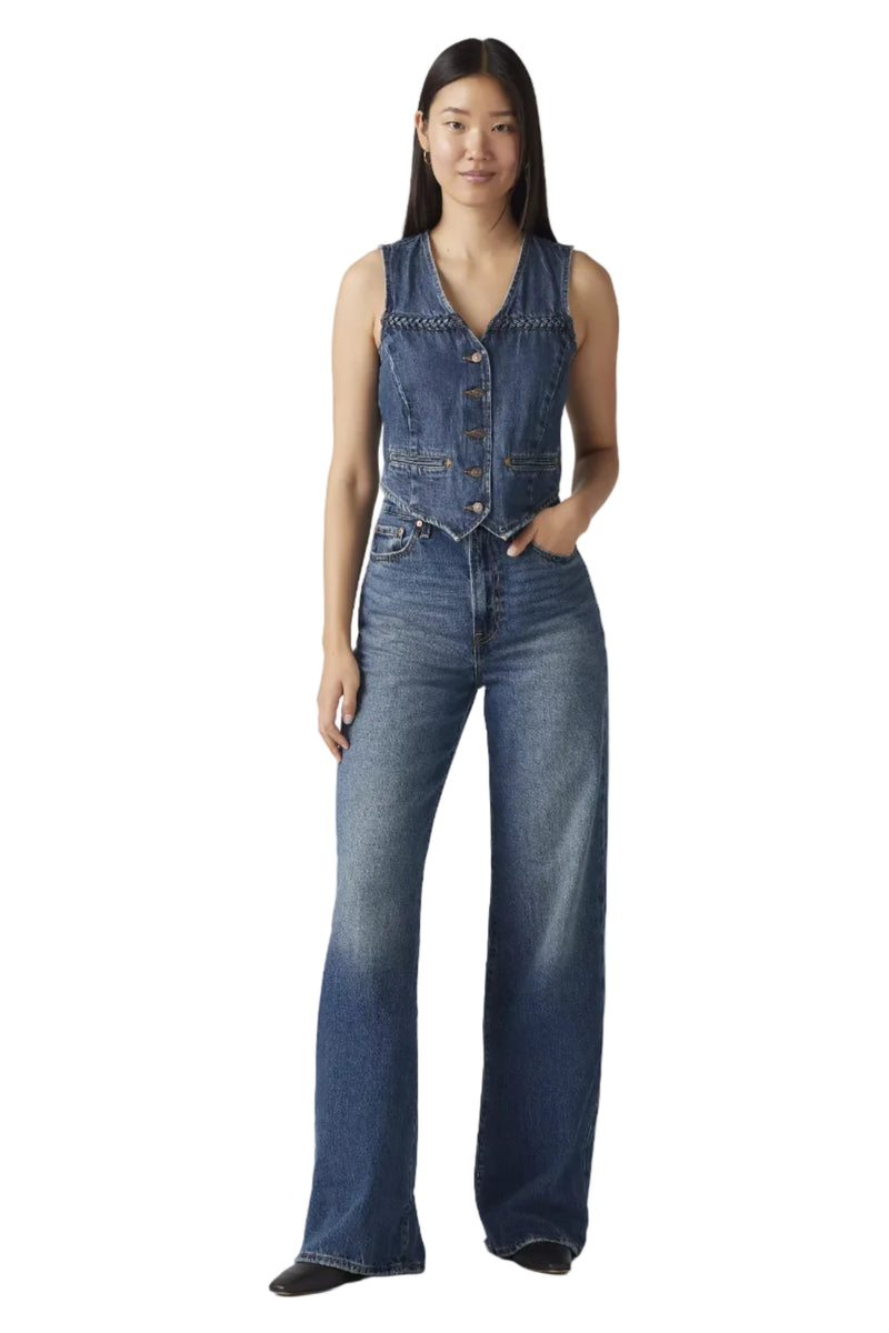 Woman wearing a denim vest and jeans on a plain background