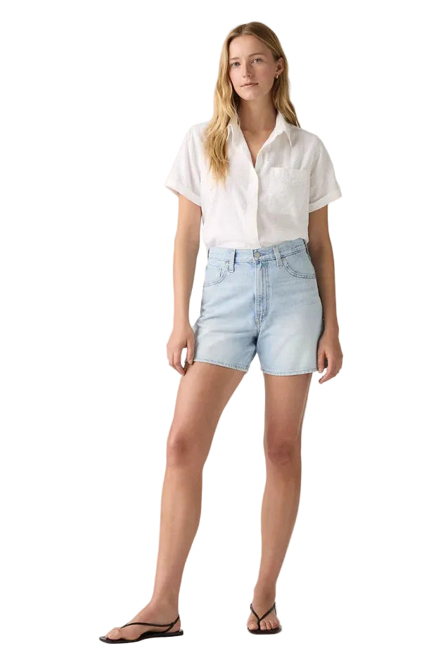 Woman wearing a white shirt and light blue denim shorts on a plain background