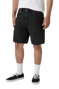 A person wearing black denim shorts, white crew socks, and black low-top sneakers against a plain light gray studio background.