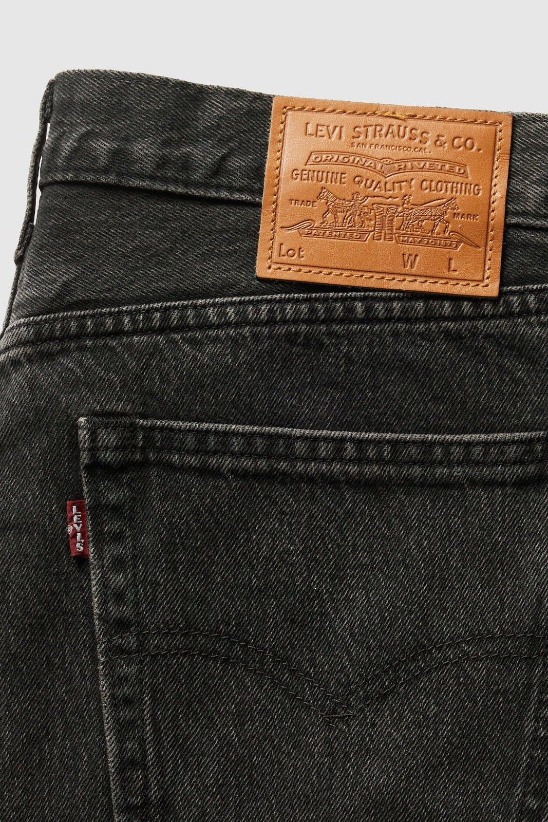 Close-up of the back waistband of Levi's 501 jeans in washed black denim, showing the signature brown leather patch with the brand name and a small red tab on the pocket.