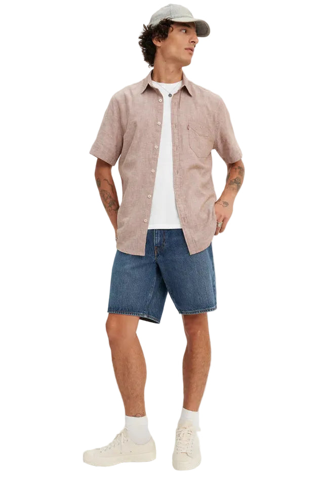 Man wearing a beige shirt, white t-shirt, blue shorts, and a cap on a white background