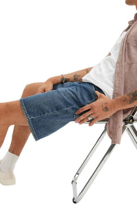 Person sitting on a chair wearing blue denim shorts and white sneakers with a plain background
