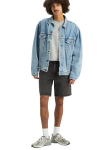 Man wearing a light blue denim jacket, gray shirt, black shorts, and white sneakers on a white background