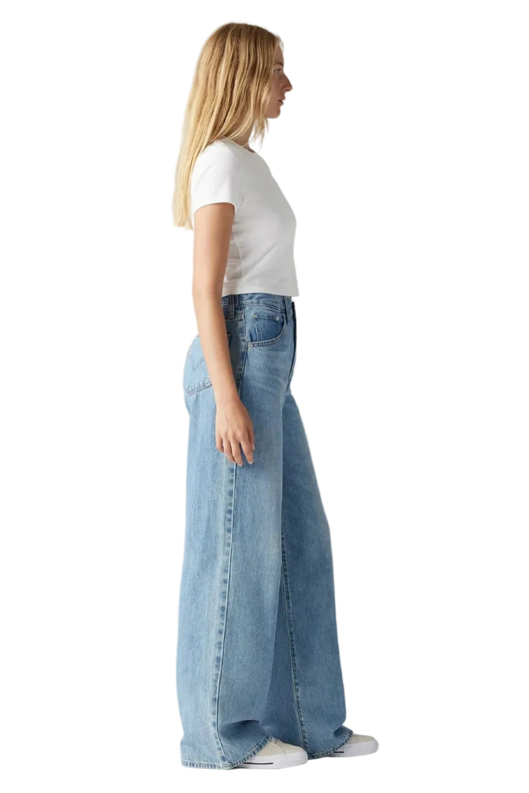 Woman wearing light blue jeans and a white top on a plain background