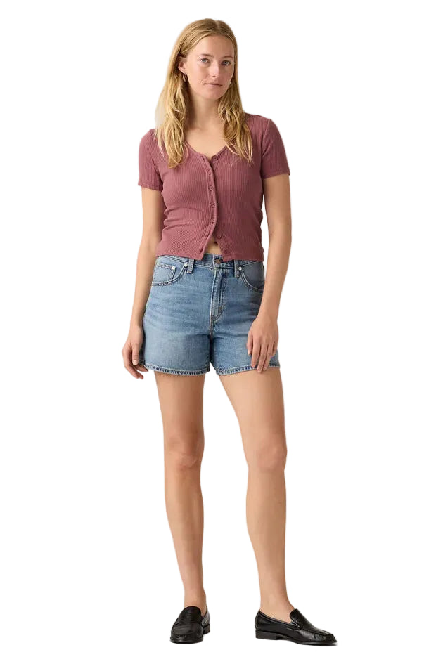 Woman wearing a pink shirt and denim shorts on a plain background