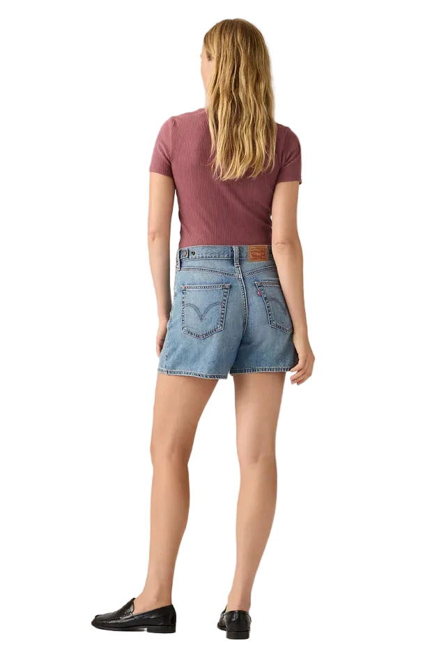 Person wearing a maroon t-shirt and blue denim shorts on a plain background