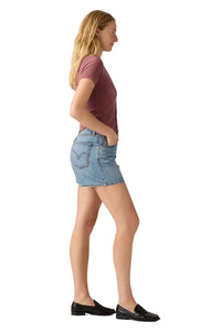 Woman wearing a maroon t-shirt and denim skirt on a plain background