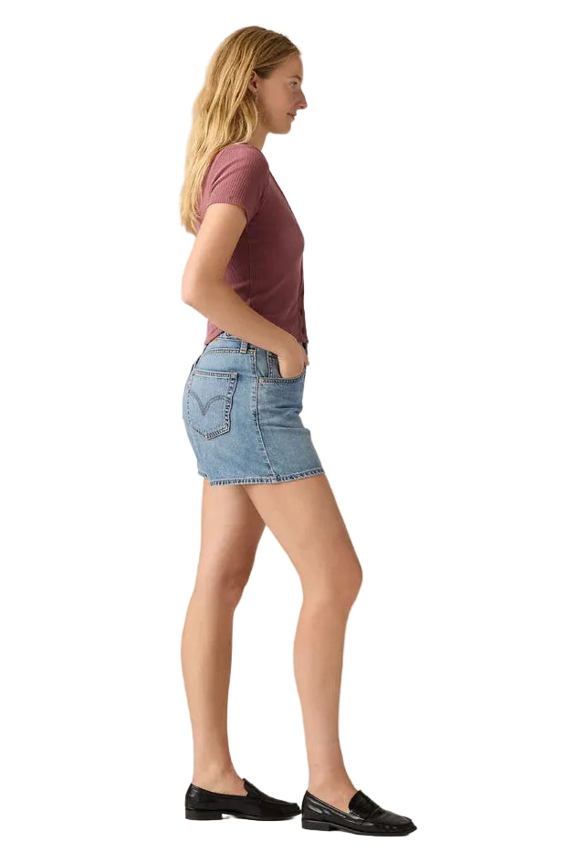 Woman wearing a maroon t-shirt and denim skirt on a plain background
