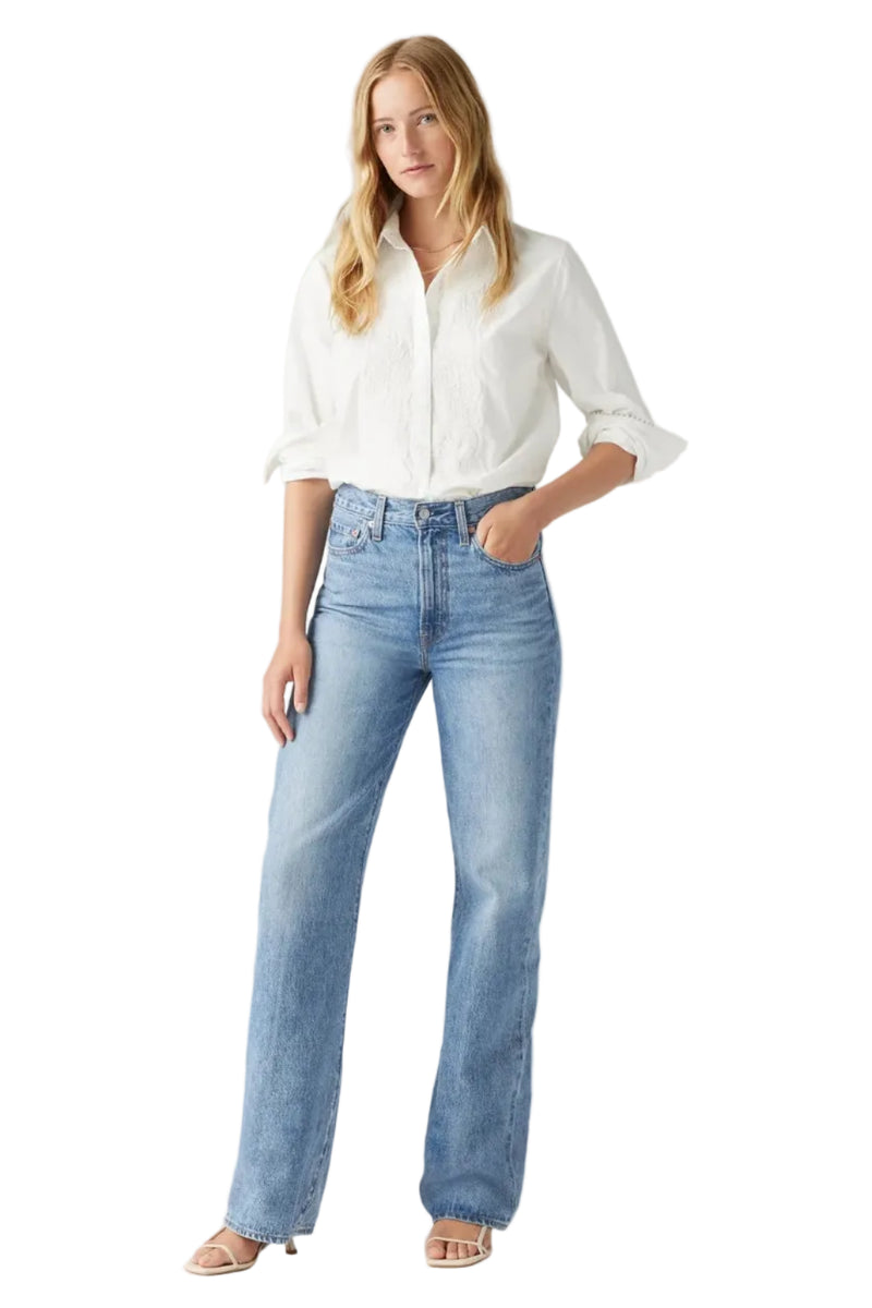 Woman wearing light blue jeans and a white shirt on a gray background