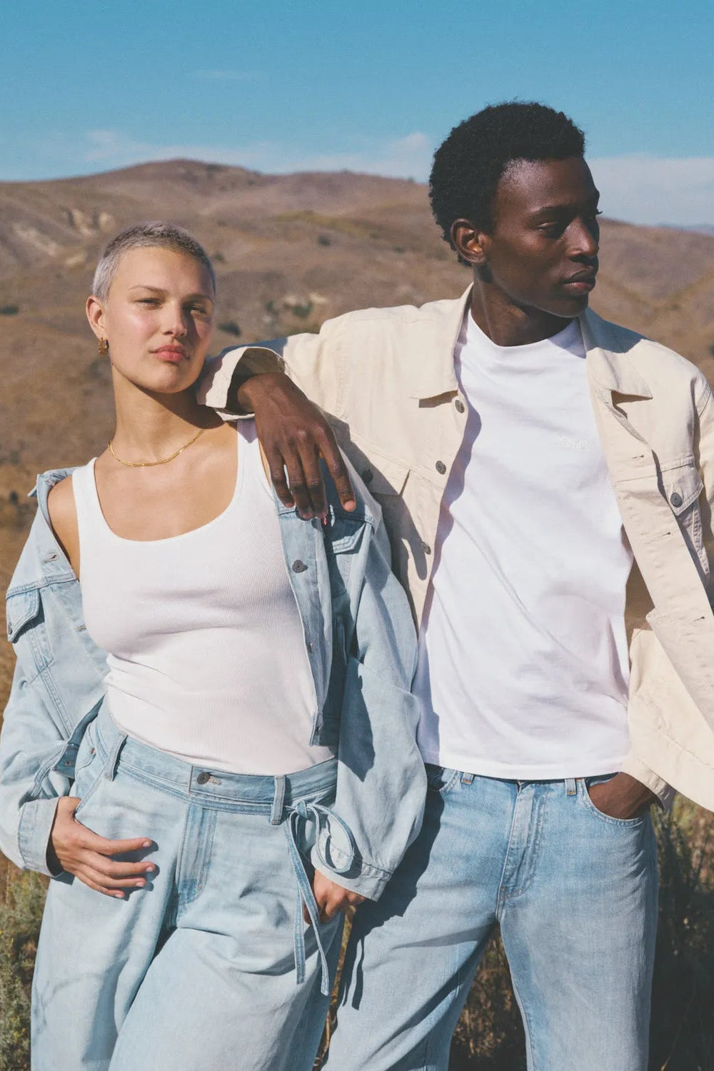 Two people standing in a desert landscape with mountains in the background
