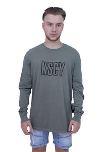 A person wearing a long sleeve khaki t-shirt with the text 'KSCY' on the front, standing against a white background.